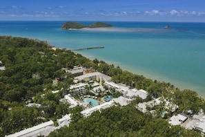 An aerial view of a resort with a swimming pool, a pier, and a beach.