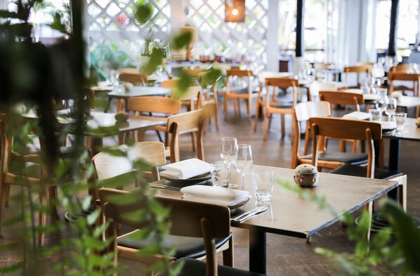 Un restaurant avec des tables et des chaises en bois, certaines mises avec des assiettes et des verres.