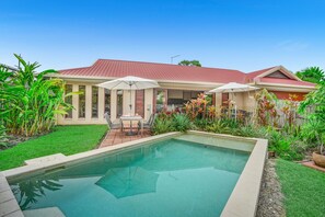 Une propriété résidentielle dotée d’une piscine, d’un patio avec mobilier d’extérieur et d’un jardin bien entretenu.