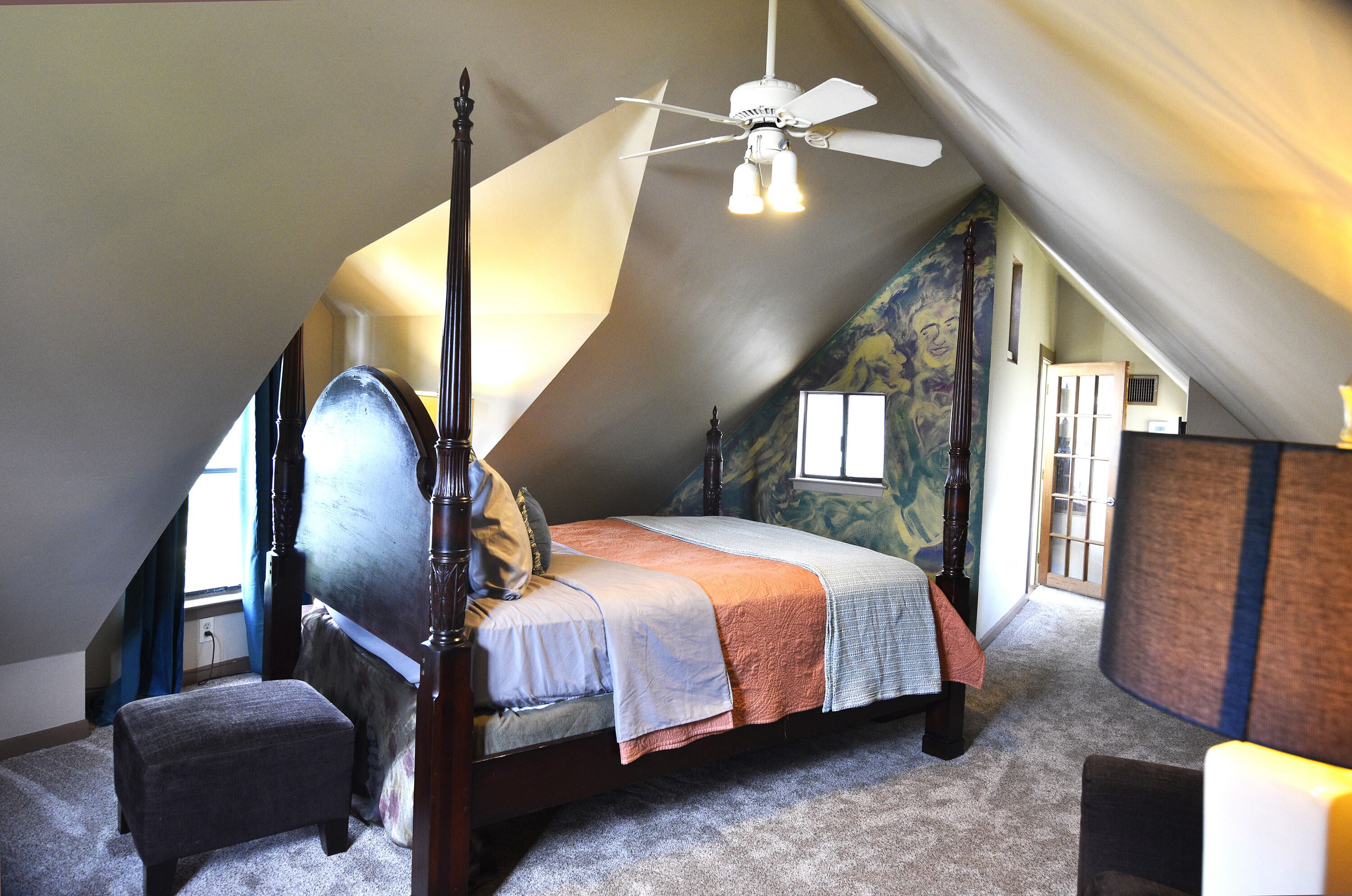 A bedroom with a four-poster bed, a ceiling fan, and a window with curtains.