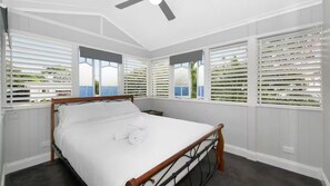 A bedroom with a bed, a ceiling fan, and windows with blinds.