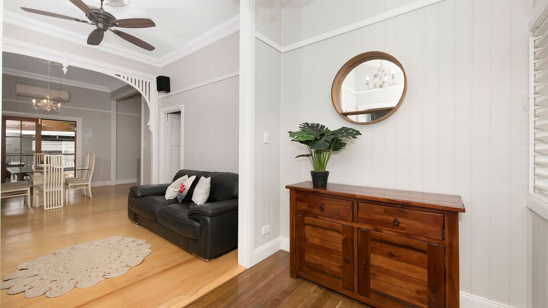 A living room with a black leather sofa, wooden dresser, and a potted plant.