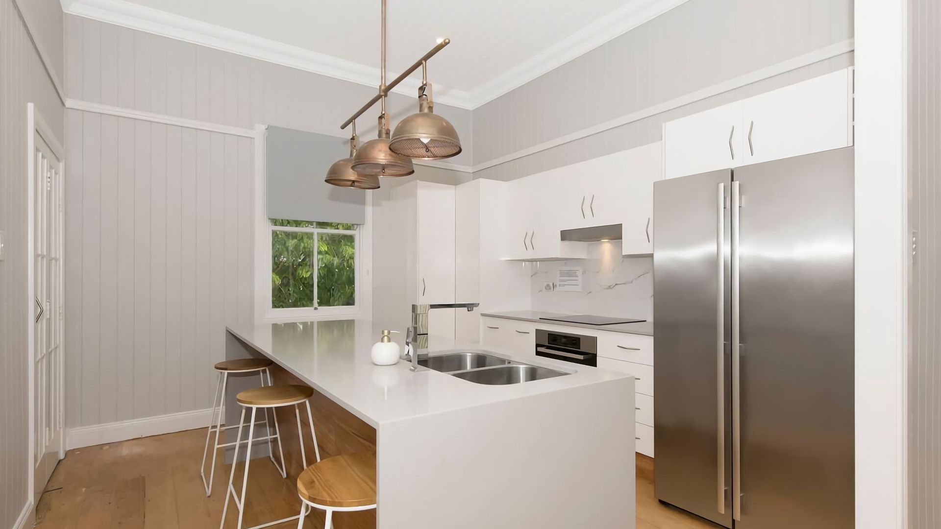A modern kitchen with a central island, stainless steel appliances, and a view of greenery outside.
