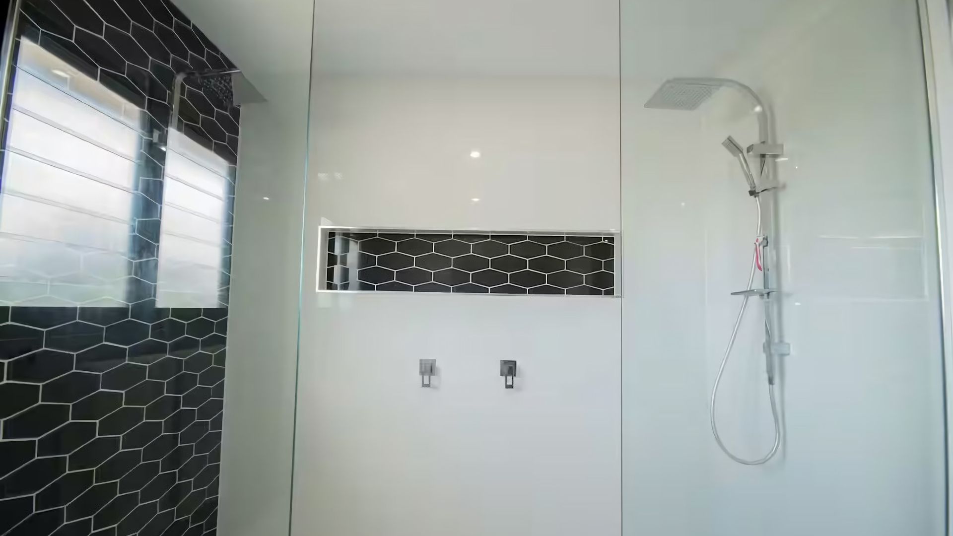 A modern bathroom with a glass shower enclosure, a black and white tiled wall, and a rectangular mirror.