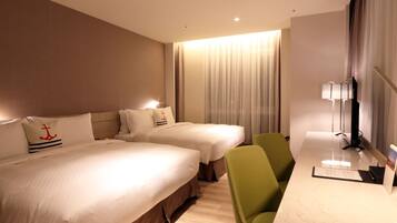A hotel room with two beds, a desk, a chair, and a lamp.