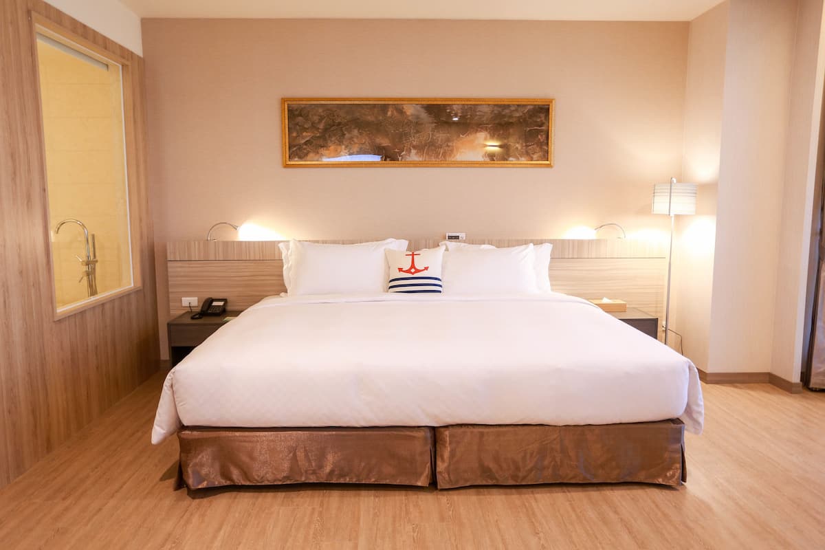 A hotel room with a large bed, wooden floor, a painting on the wall, and two bedside lamps.