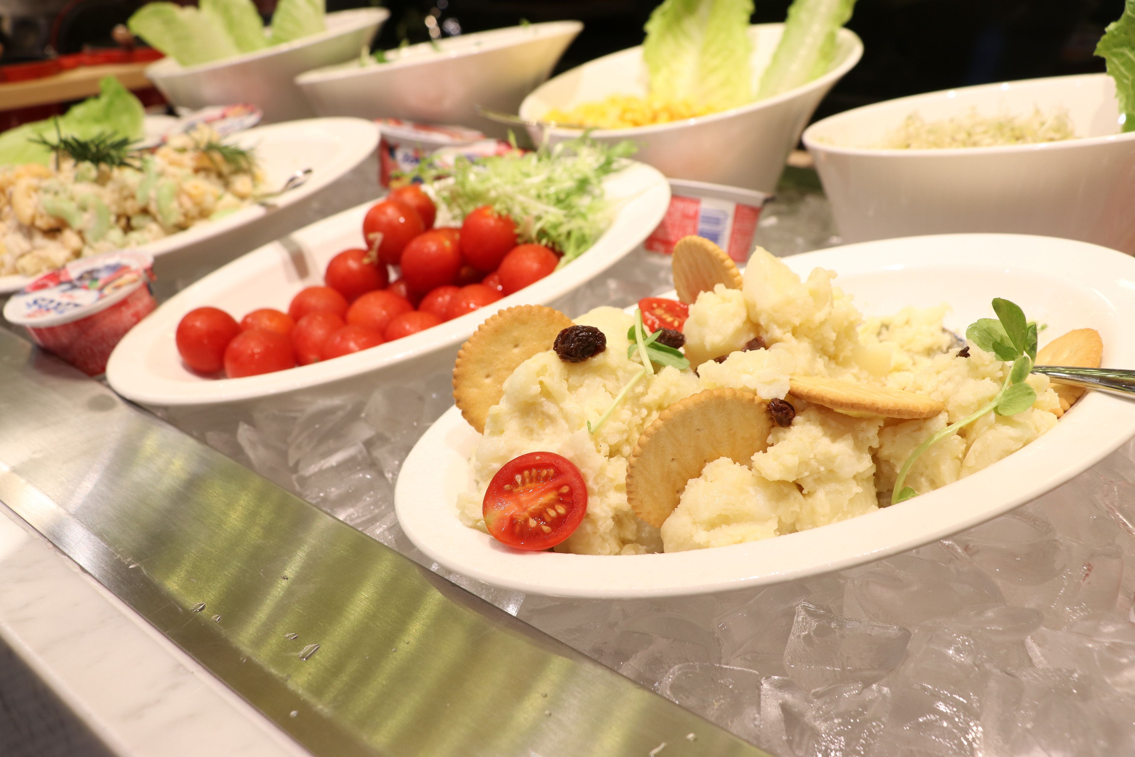 Un bufé con diversos platos, entre ellos puré de patatas, tomates cherry y otras ensaladas.