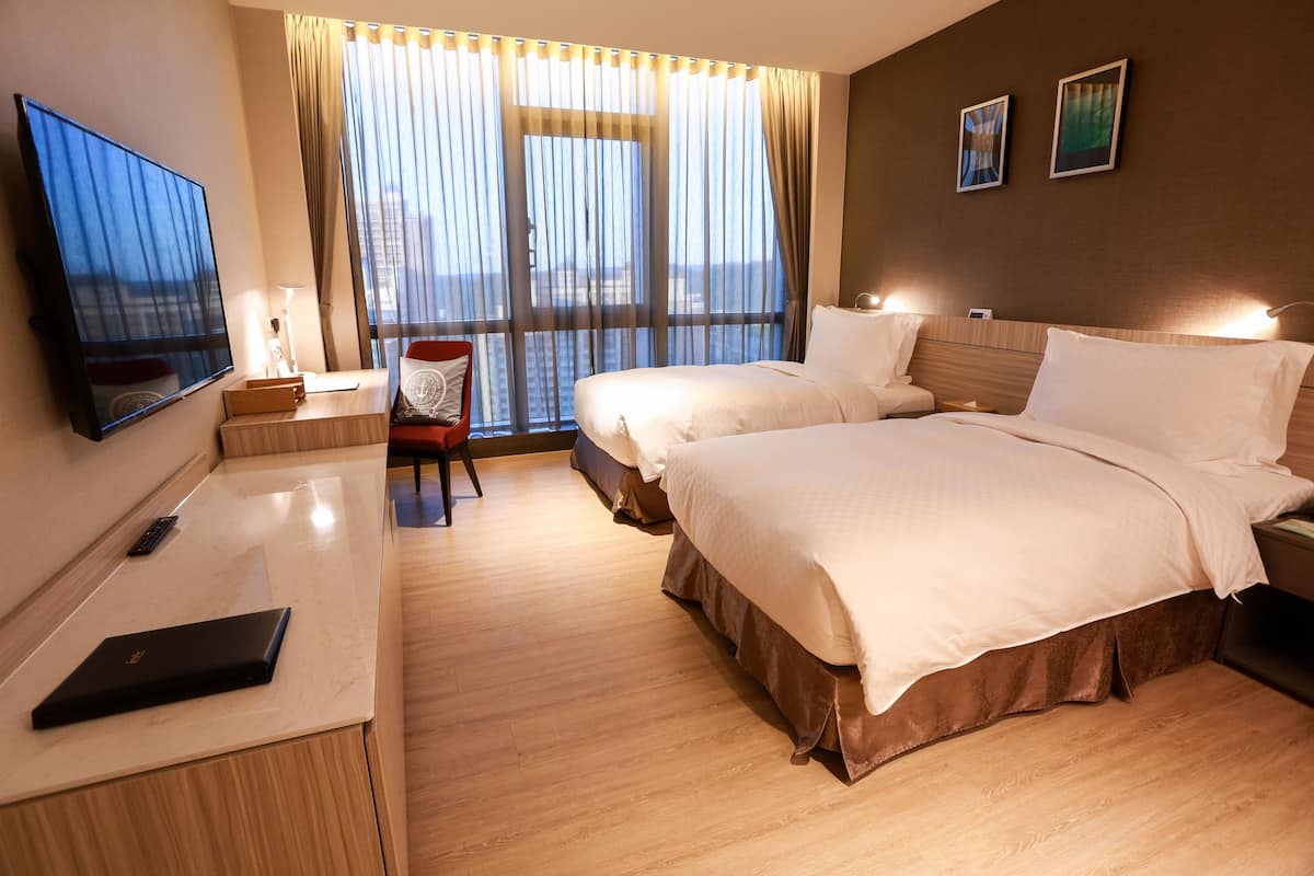 A hotel room with two beds, a desk with a laptop, a TV, and a chair.