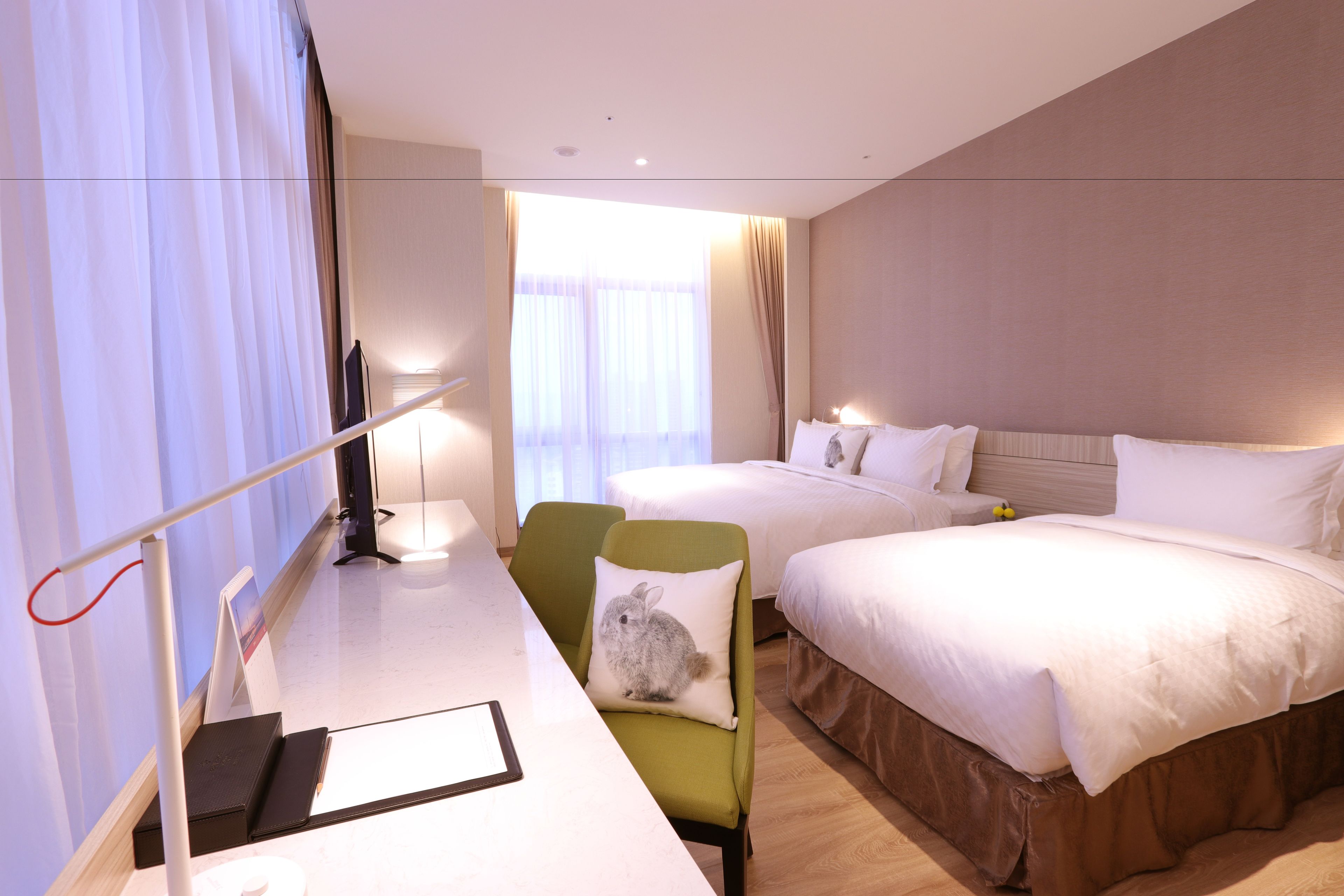 A hotel room with two beds, a desk with a chair, a television, and a window with curtains.