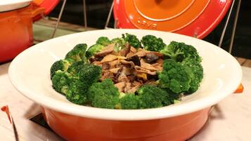 A large orange serving dish filled with beef and broccoli, placed on a white plate.
