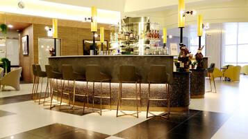 A modern bar area with a central bar counter, multiple stools, and a decorative display of bottles and glasses.