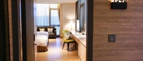 A hotel room with a bed, a chair, a desk, and a large window.