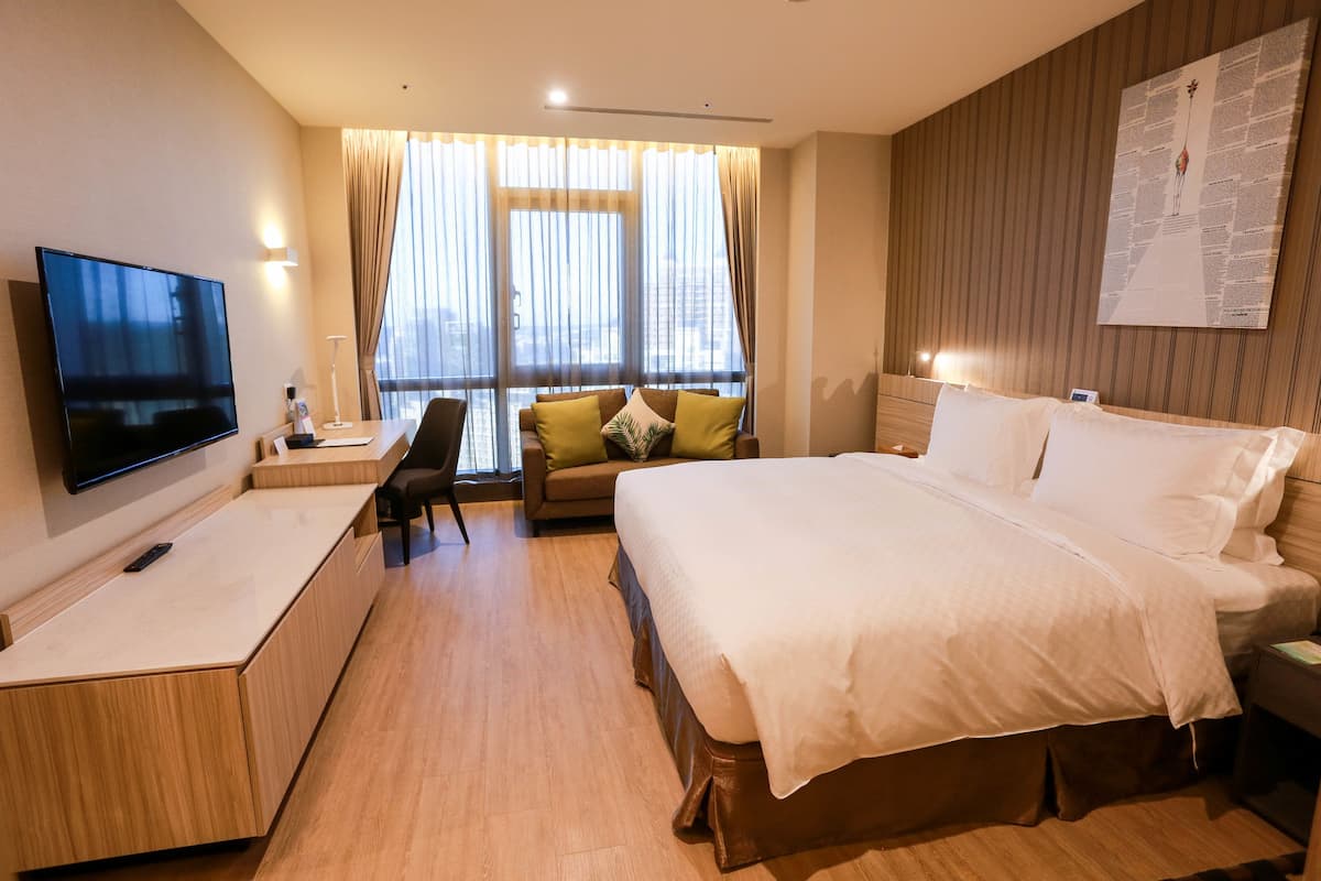 A hotel room with a large bed, a TV, a desk, and a sofa.