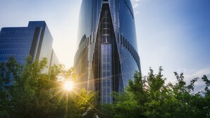 A modern skyscraper with a curved glass facade, surrounded by lush green trees. - AJ Hotel Hsinchu (Zhubei)