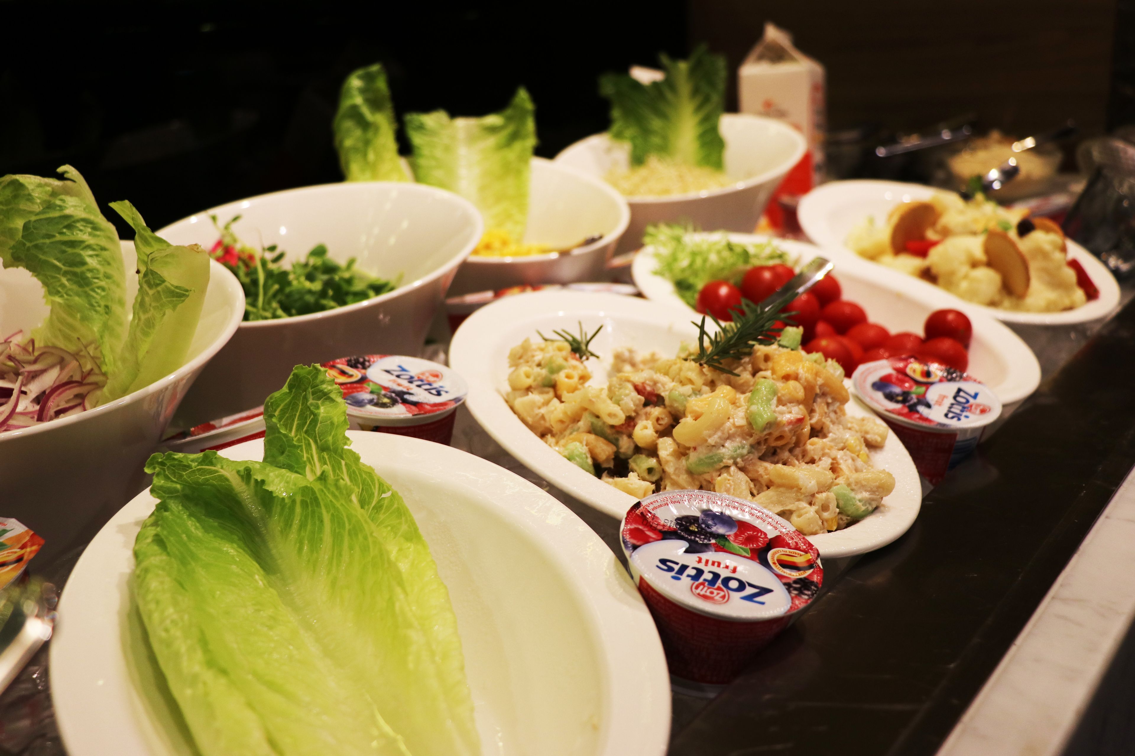 A buffet table with various dishes including salads, pasta, and yogurt cups.