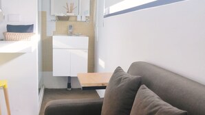 Un espai vital reduït amb un sofà, una taula petita, una cadira i una zona de cuina sense voler.