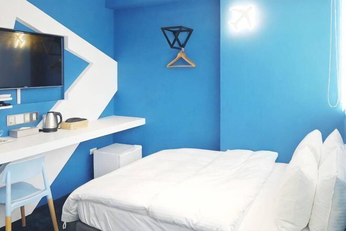 Una habitación con cama, escritorio, silla, televisor y lámpara colgante.