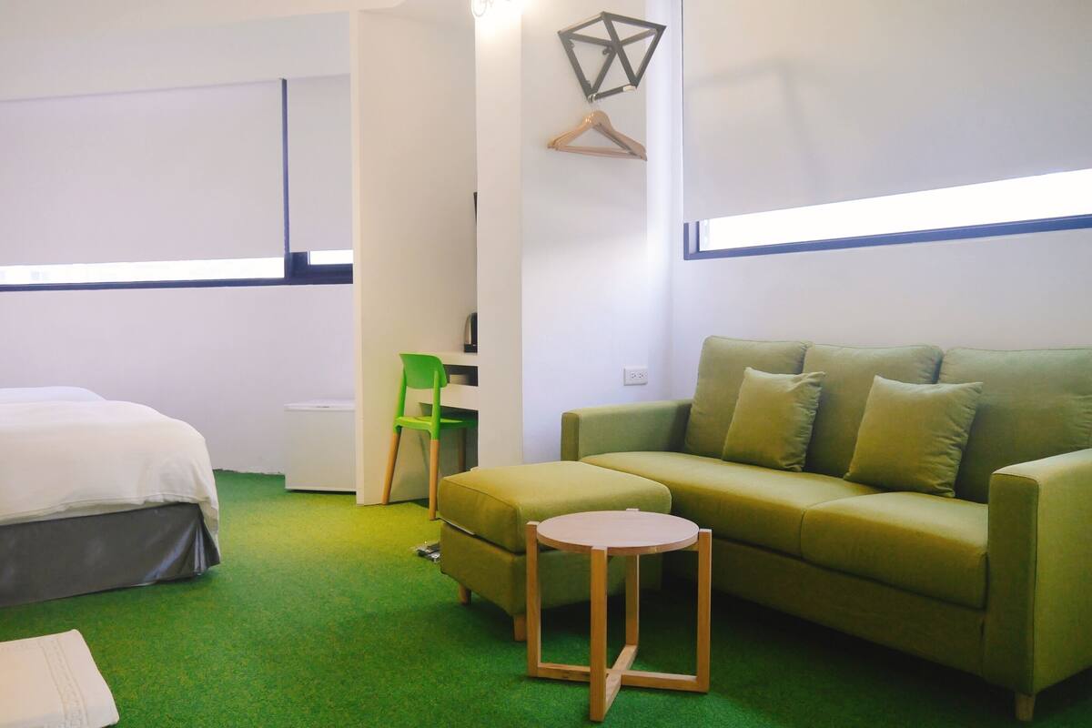 Habitación con cama, sofá verde, una mesita, una silla y un perchero de pared.