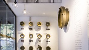 Un interior modern amb una col·lecció de rellotges a la paret, una taula central amb un vas i una escala amb barana negra.