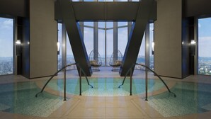 Un área de piscina interior moderna con vistas despejadas al paisaje urbano a través de amplios ventanales.