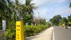 A yellow sign with 'KM 114' on a road with palm trees and a clear sky. - Luzmin BH - Beachfront Cottages (Oslob)