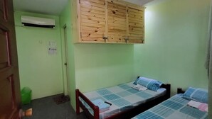 A room with two beds, a wooden wardrobe, an air conditioning unit, and a green trash bin. - Luzmin BH - Beachfront Cottages (Oslob)