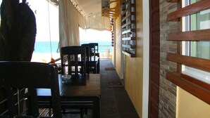 A corridor with a view of the sea, wooden chairs and tables, and a stone wall with a wooden door. - Luzmin BH - Beachfront Cottages (Oslob)