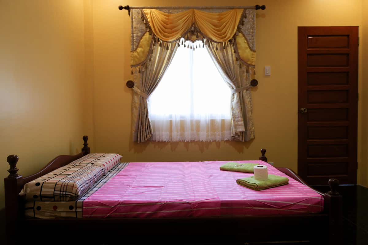A bedroom with a bed, a window with curtains, a door, and a wall with a light switch.