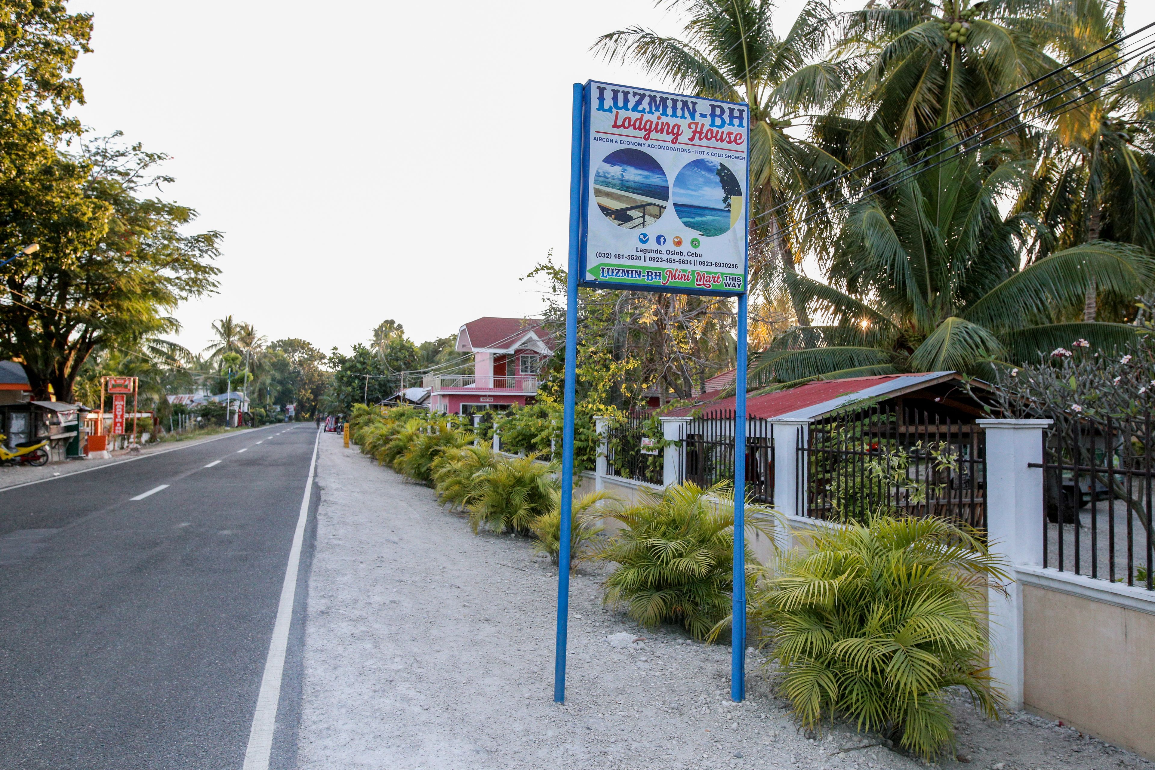 A sign for a lodging house with a view of the beach and palm trees.