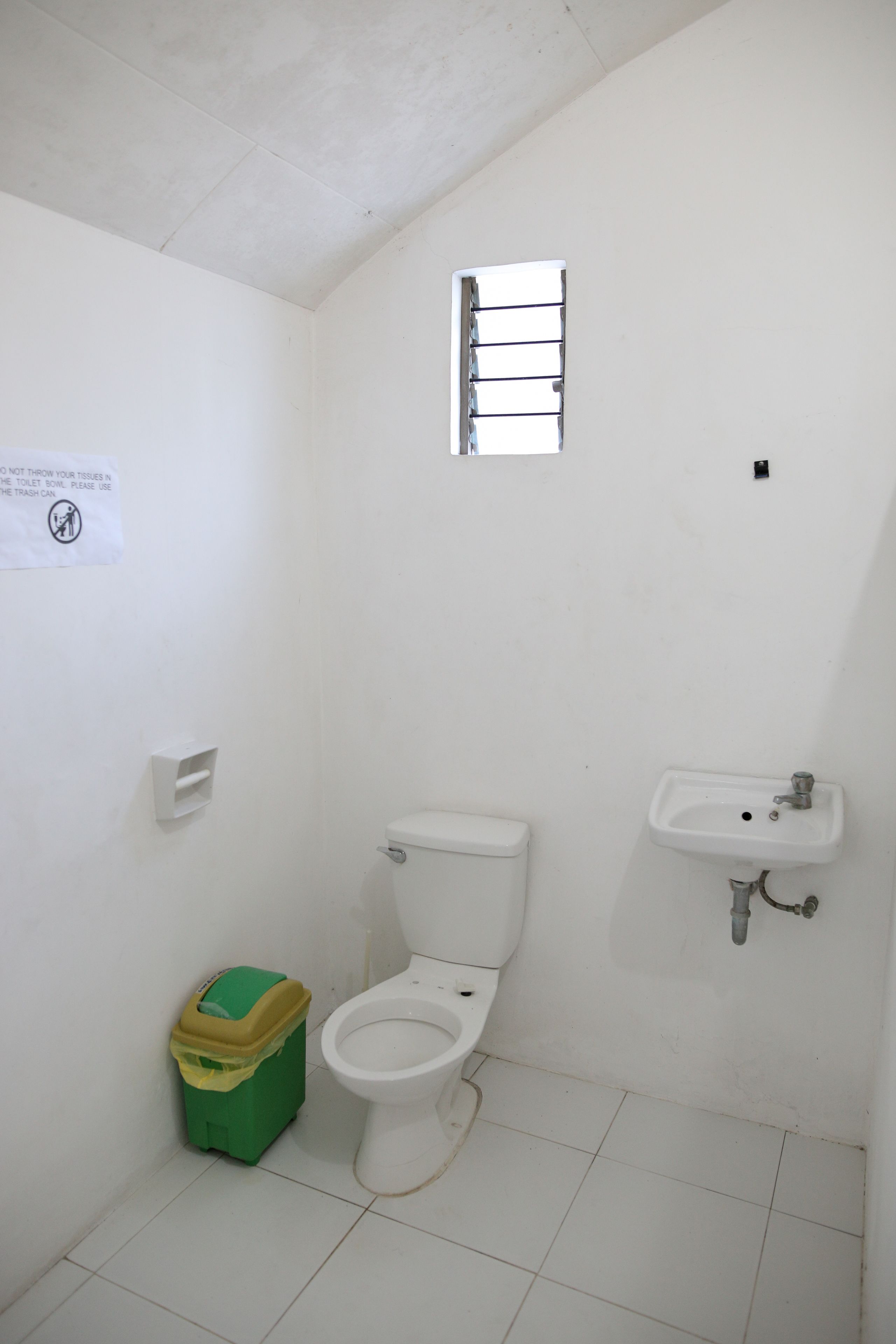 A small, white bathroom with a toilet, a sink, and a trash bin.