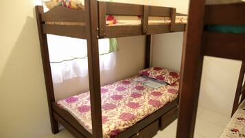 Un lit superposé avec une couvre-lit à motifs floraux, un seul tiroir et une fenêtre avec un rideau.