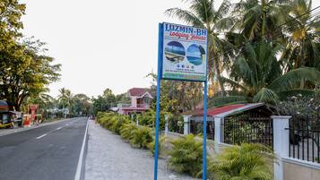 A sign for a lodging house with a view of the beach and palm trees.
