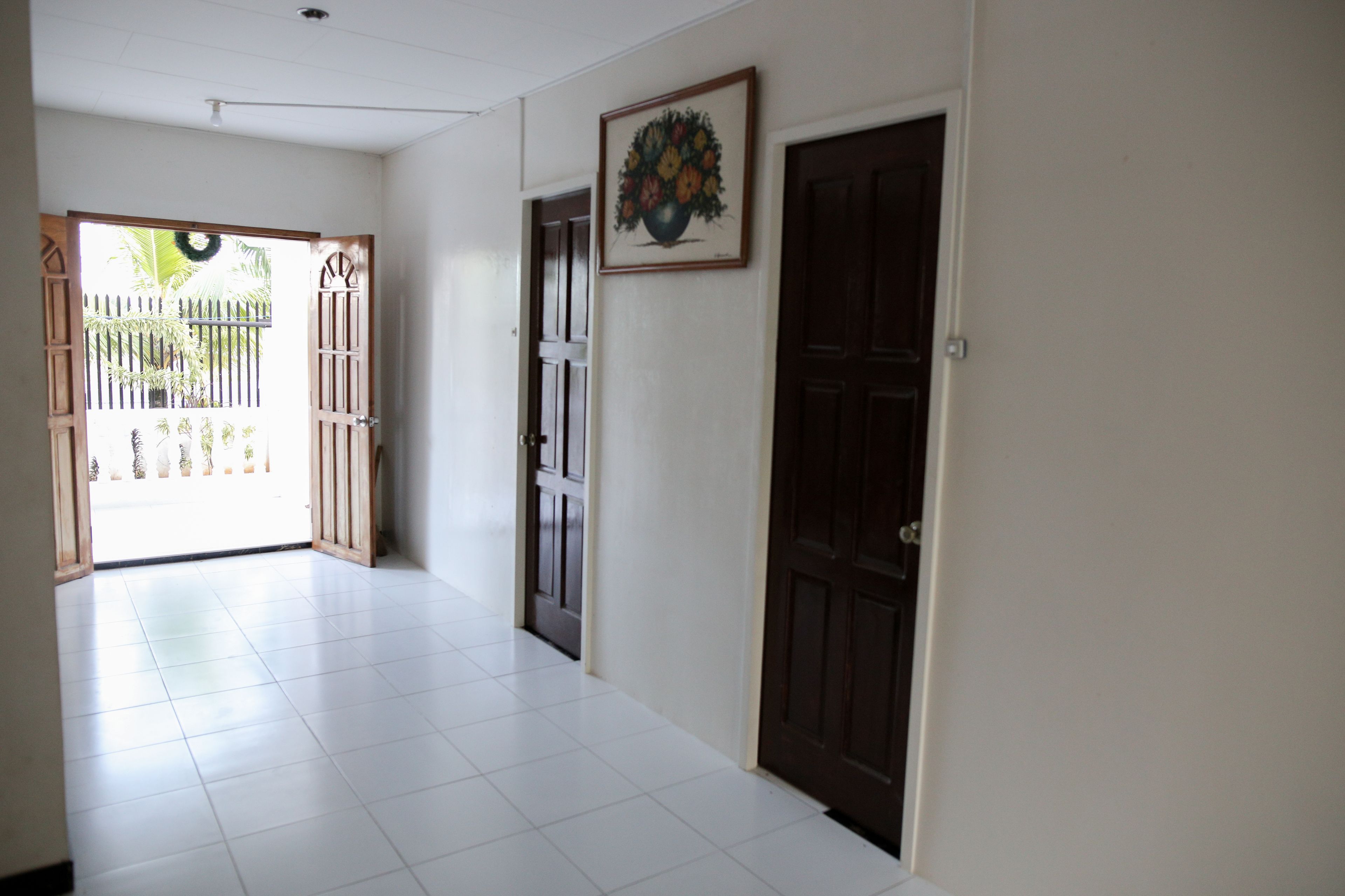 A hallway with white tiled flooring, a wooden door, and a framed picture on the wall.