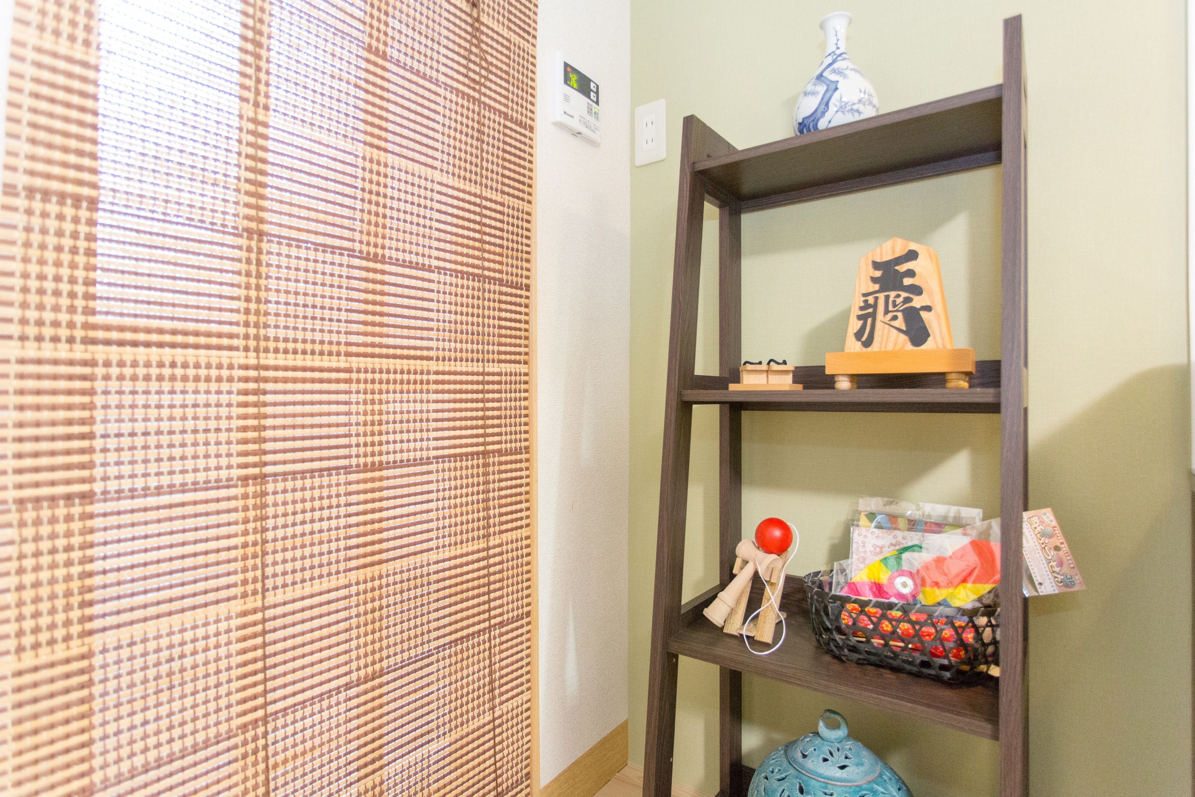 A room with a bamboo blind, a wooden shelf with decorative items, and a blue ceramic pot.