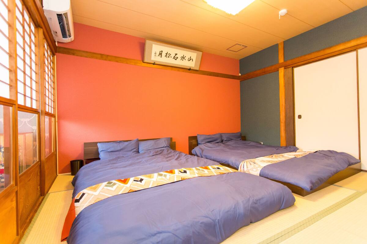 A hotel room with two beds, a tatami mat floor, a ceiling fan, and a sign with Japanese characters.
