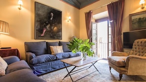 Un salon avec un canapé, un fauteuil et une table basse. Il y a un tableau au mur et une plante sur la table.