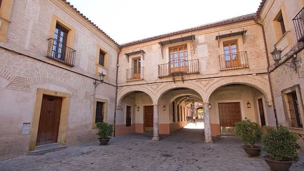 Une cour dallée de pierres, agrémentée d’arcades et de plantes en pot.