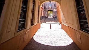 Un couloir aux plafonds en arc de cercle et au sol pavé de pierres menant à l’entrée d’un bâtiment.