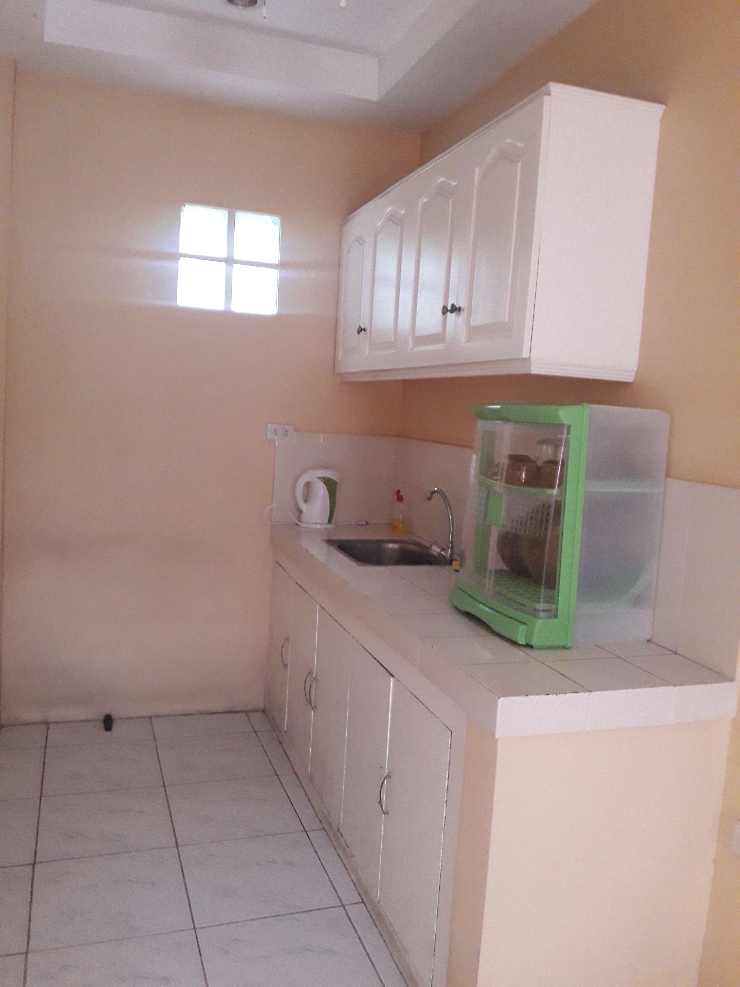 A small kitchen with white cabinets, a sink, and a green appliance on the counter.