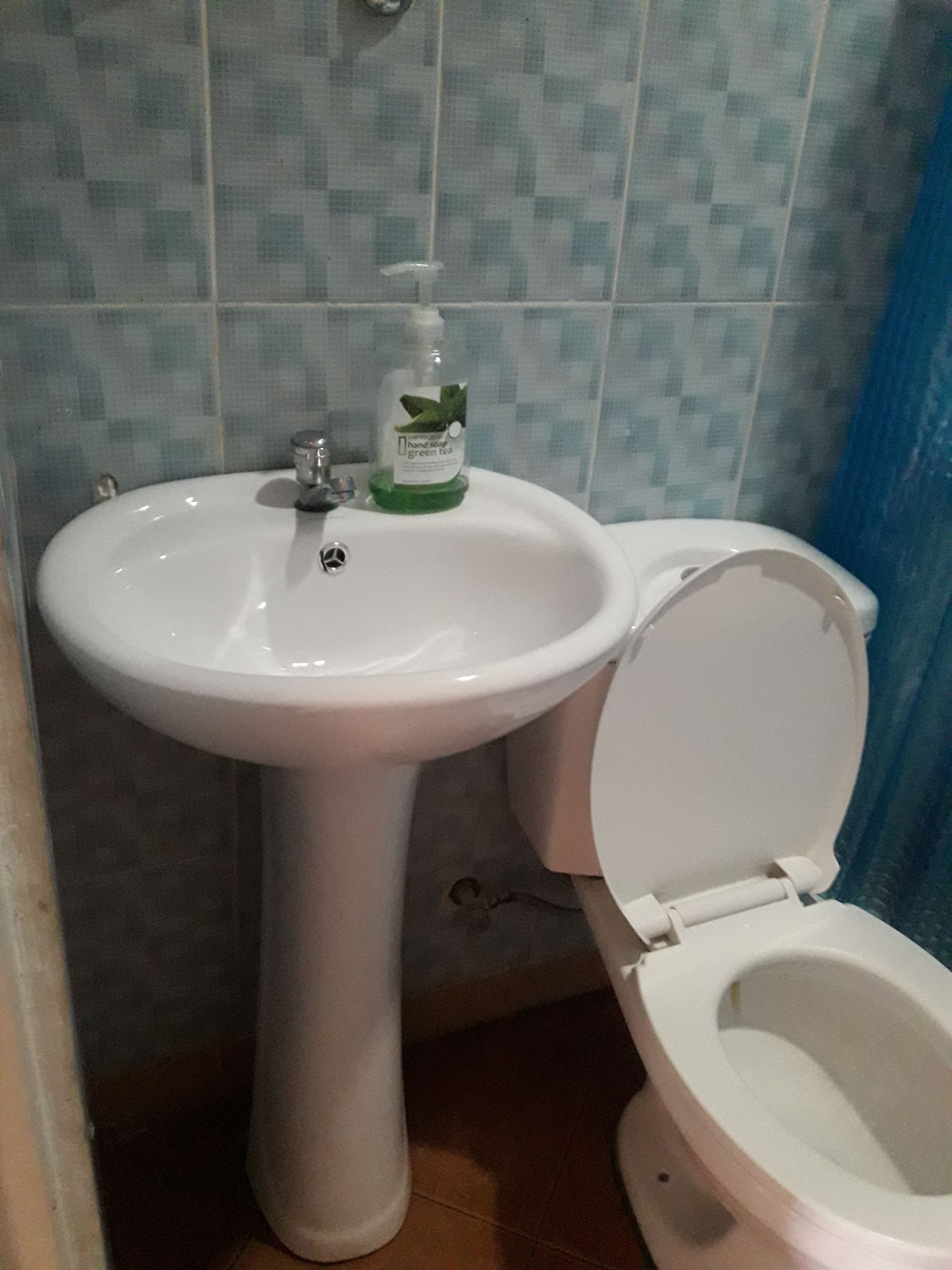 Ein Badezimmer mit einem weißen Waschtisch, einer Toilette und einem Handseifenspender auf dem Waschbecken.