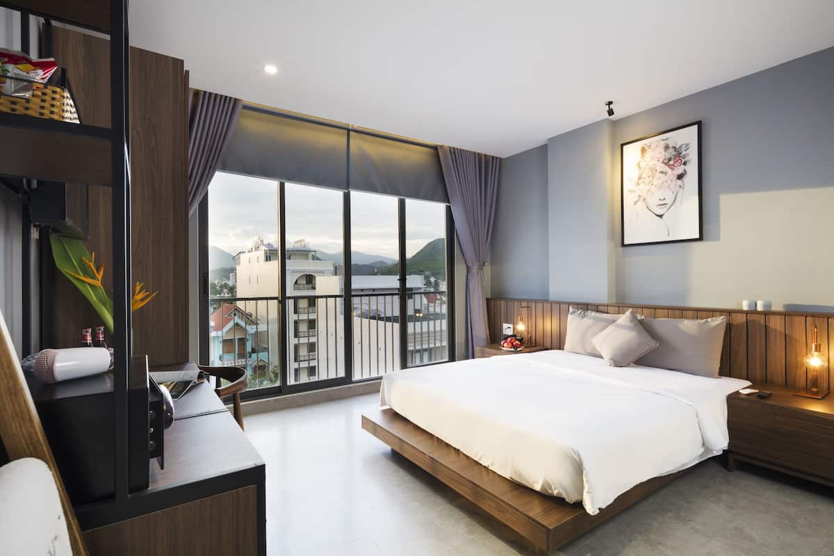 Una habitación de hotel moderna con una cama grande, un escritorio y vistas a la ciudad a través de amplios ventanales.