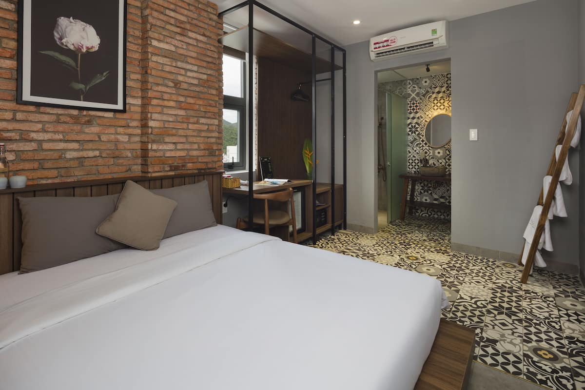 Habitación de hotel con una cama grande, un escritorio, una silla, un espejo y un baño con baldosas estampadas.