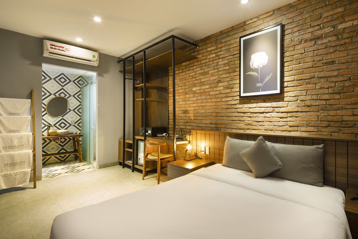 Habitación de hotel con una cama grande, un escritorio con una silla, un espejo y una pared de ladrillo.