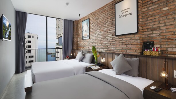 A hotel room with two beds, a brick wall, a large window, and a view of buildings. - Marilyn Nha Trang Hotel (Bac Nha Trang)