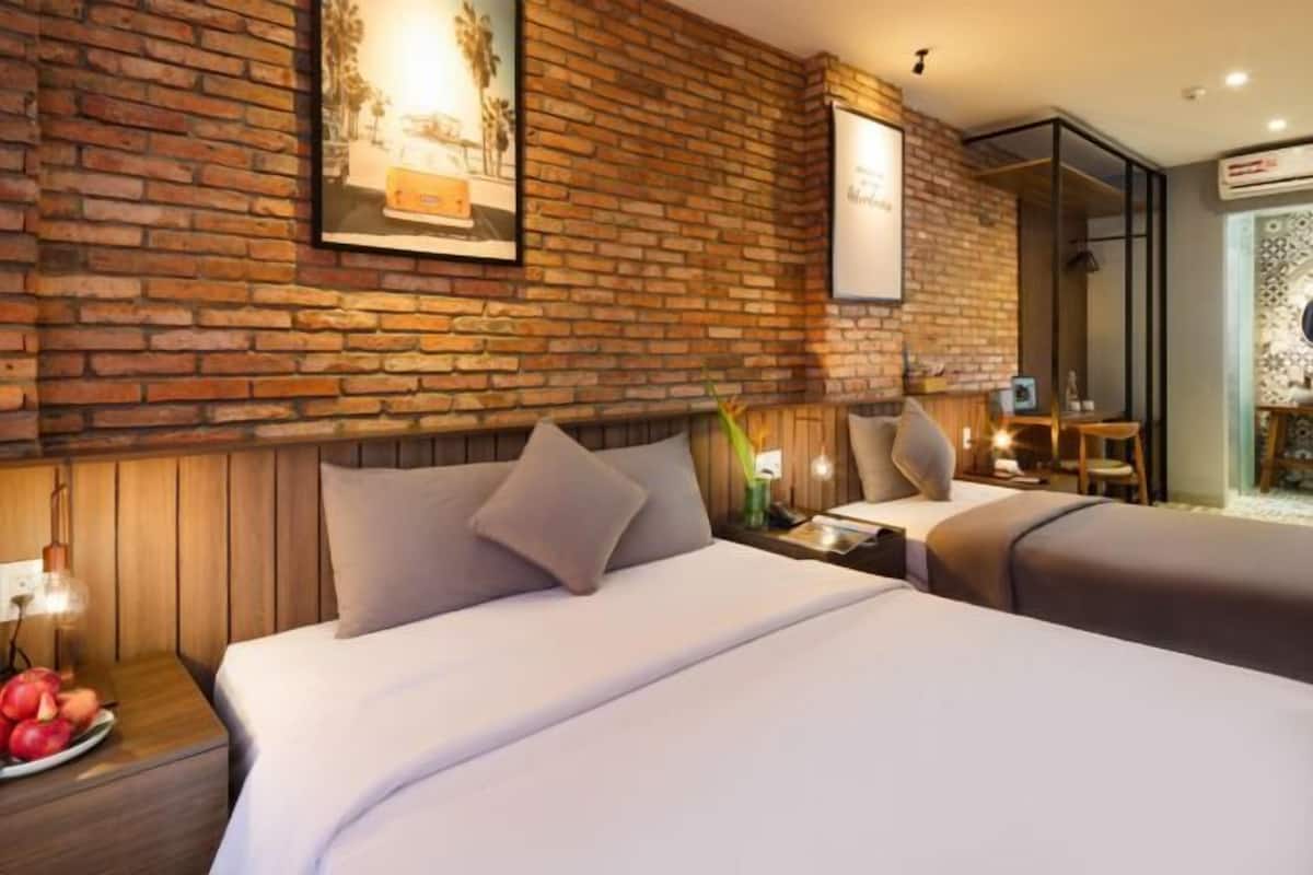 Una habitación de hotel con pared de ladrillo, dos camas, una mesita de noche con fruta y un espejo.