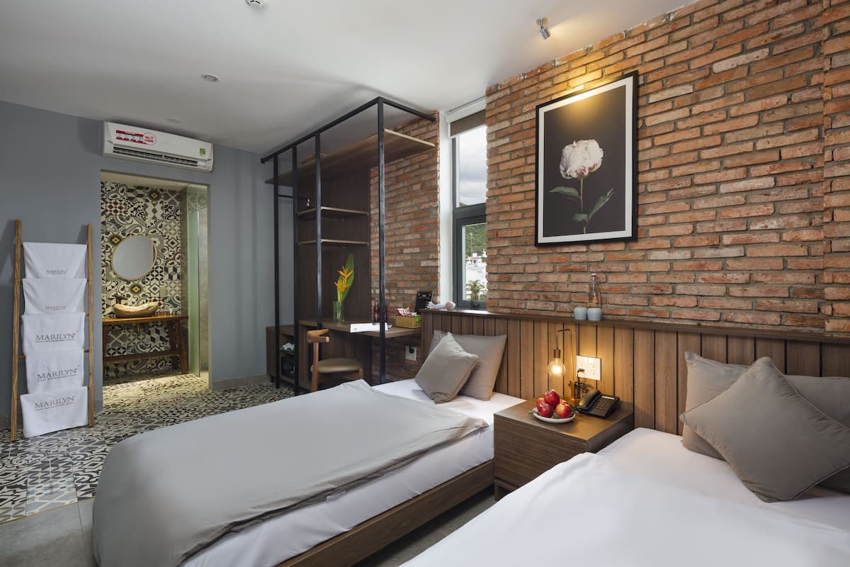 Una habitación de hotel moderna con pared de ladrillo, una cama, un escritorio y zona de ducha.