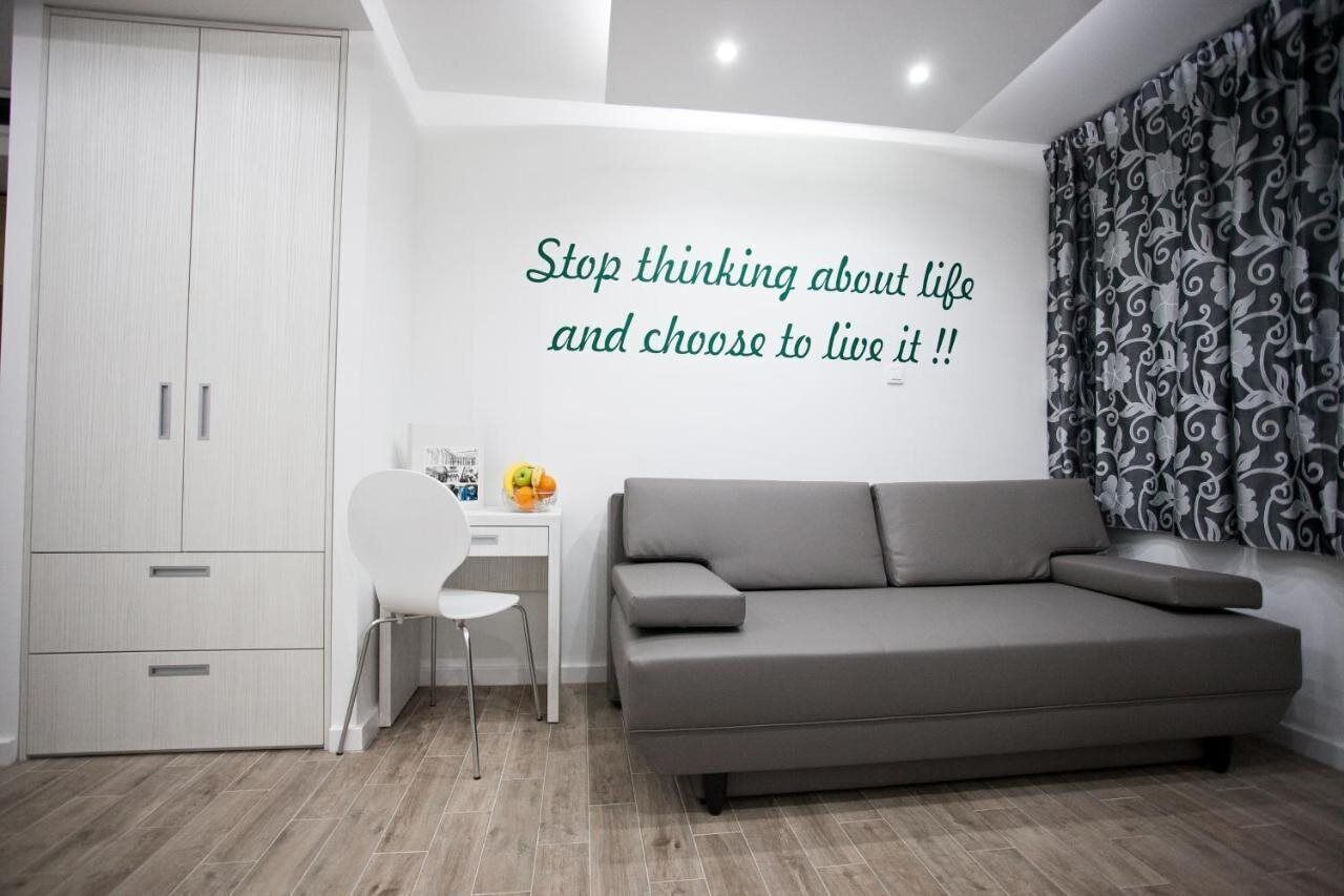 A modern living room with a grey sofa, a white desk, and a wardrobe. A motivational quote is displayed on the wall.