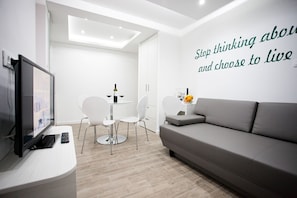 Una sala de estar moderna con un sofá gris, un televisor, una mesa de comedor con sillas y una pared con texto motivacional.