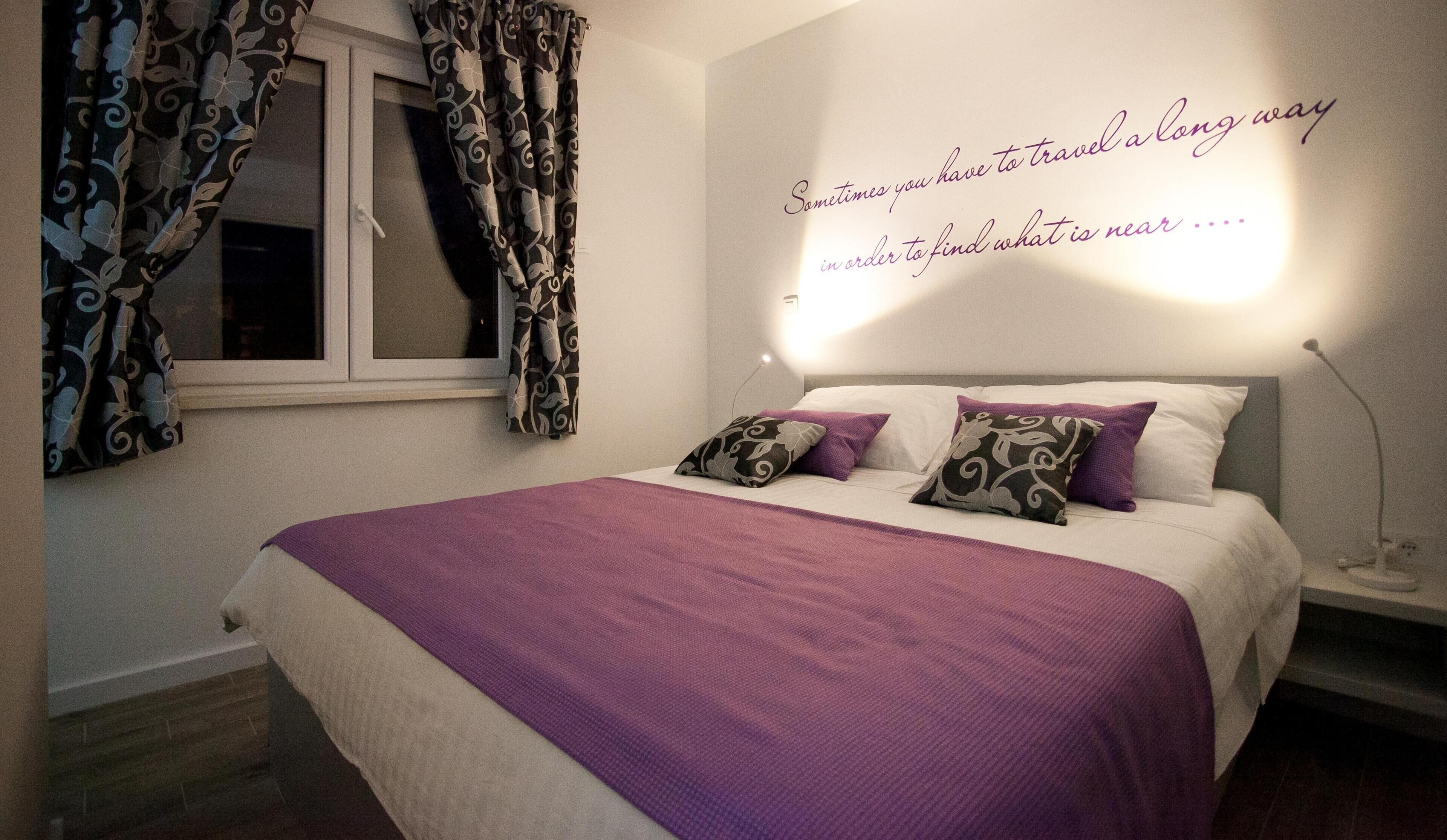 Ein Schlafzimmer mit einem Bett, Vorhängen, einer Wand mit einem Zitat und einer Nachttischlampe.