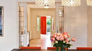 A dining area with a dark wooden table, a vase of pink roses, and a view into a room with a red curtain.